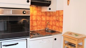 A compact kitchen with a built-in oven, a dishwasher, and a sink with a wooden countertop.