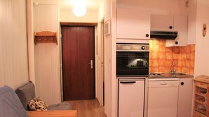 A compact kitchen with a built-in oven, a dishwasher, and a sink. There is a wooden cabinet with a microwave above the sink. A small wooden table is next to the sink.