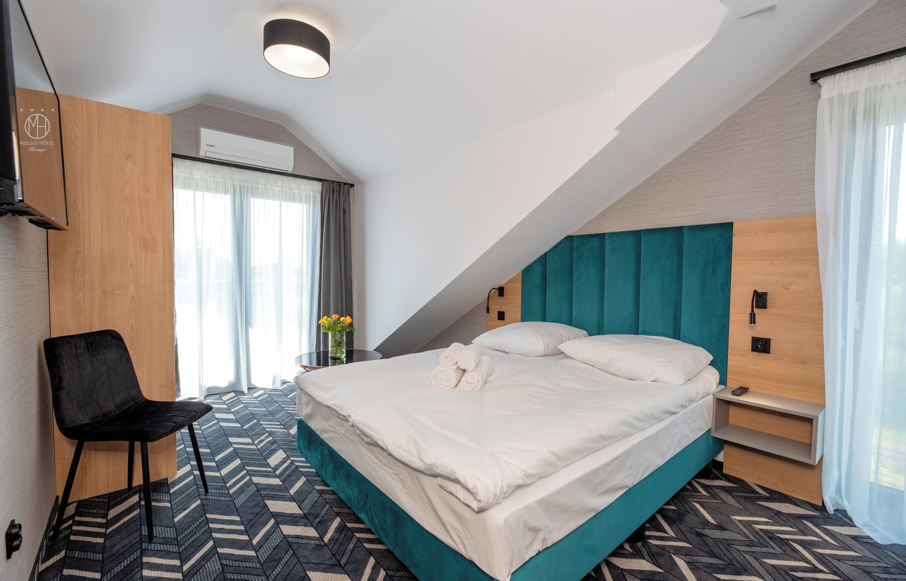 Hotellihuone, jossa on sänky, tuoli, työpöytä ja ikkuna, jossa on verhot.
