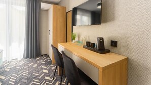 A hotel room with a wooden desk, a flat-screen TV mounted on the wall, a coffee maker, and a potted plant. - Mielno Hotel Boutique (Mielno)