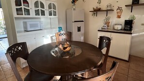 A dining area with a round table and chairs, a white cabinet with glass doors, a white refrigerator, and a wall-mounted painting. - Mariposa End Unit Loft (Playas Del Coco)