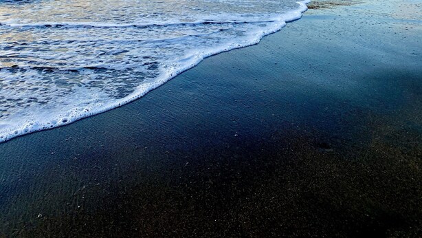 A beach with waves, a sailboat, and a distant island. - Mariposa End Unit Loft (Playas Del Coco)