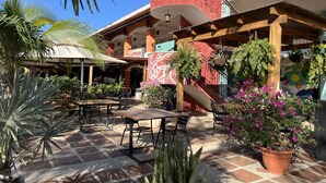 An outdoor patio area with tables and chairs, surrounded by potted plants and a mural. - Mariposa End Unit Loft (Playas Del Coco)