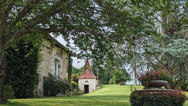 A stone building with a small tower, surrounded by lush greenery and a well-maintained lawn. - Charming Gîte with Heated Pool, Garden, BBQ, and Baby Equipment Near Aubeterre-sur-Dronne (Bellon)