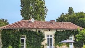 A house with a tiled roof, ivy-covered walls, a satellite dish, and a patio with a table and chairs. - Charming Gîte with Heated Pool, Garden, BBQ, and Baby Equipment Near Aubeterre-sur-Dronne (Bellon)