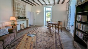 A cozy living room with exposed wooden beams, a fireplace, a coffee table, a sofa, a dining table with chairs, and a bookshelf. - Charming Gîte with Heated Pool, Garden, BBQ, and Baby Equipment Near Aubeterre-sur-Dronne (Bellon)