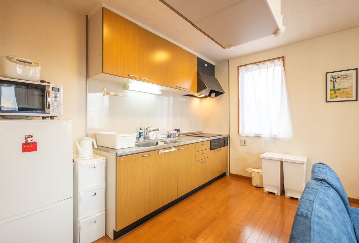 A compact kitchen with wooden cabinets, a microwave, a sink, and a small window with curtains.