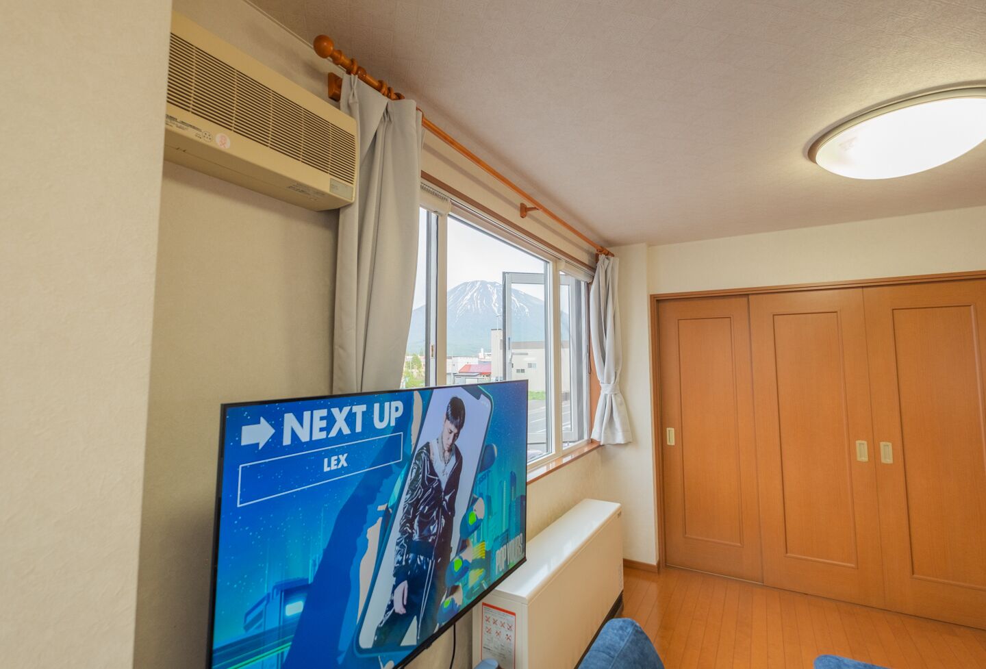 Una habitación con un ventanal grande, una puerta de madera y un televisor de pantalla plana mostrando un anuncio.
