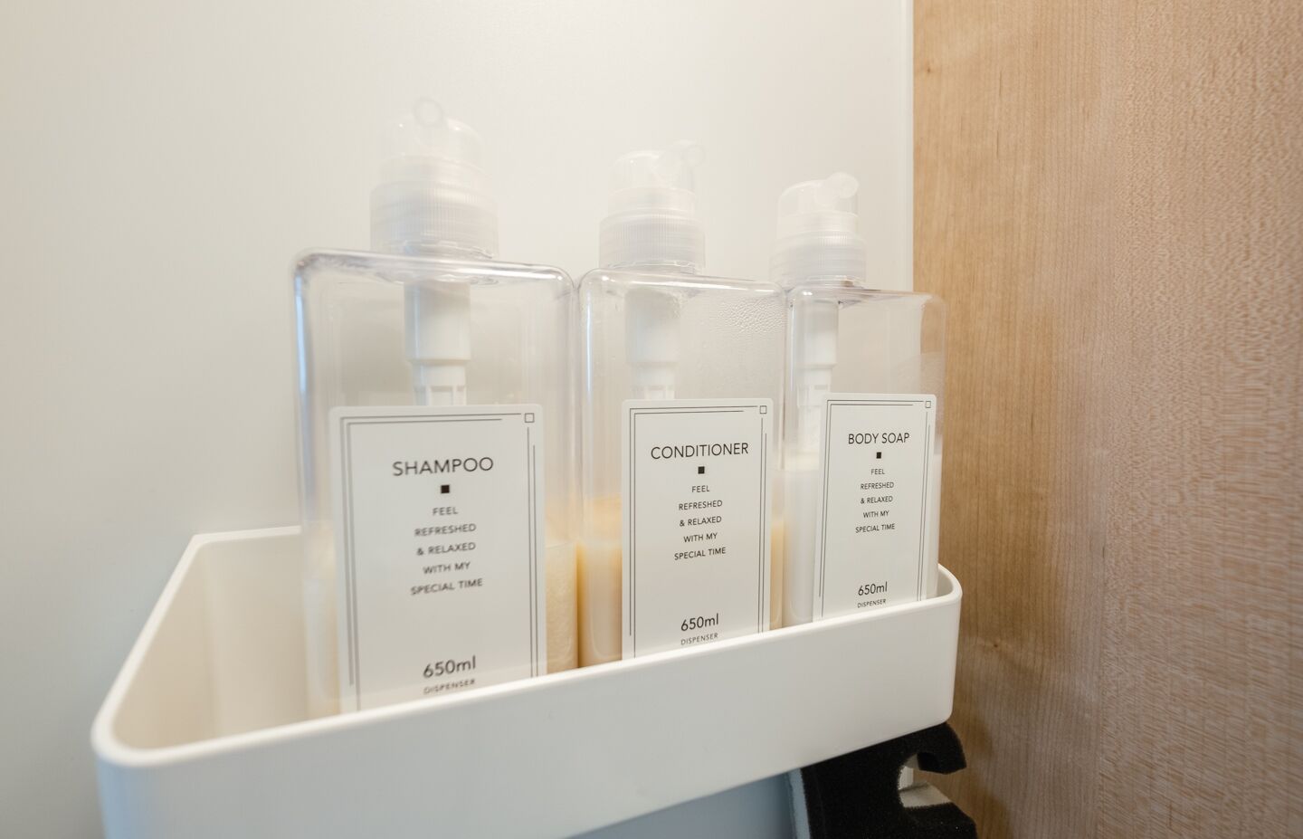 A bathroom shelf with three dispensers labeled 'Shampoo', 'Conditioner', and 'Body Soap', each with a capacity of 650ml.