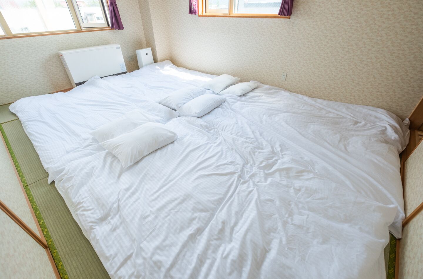 A neatly made bed with white linens, a green mat, and a white radiator.