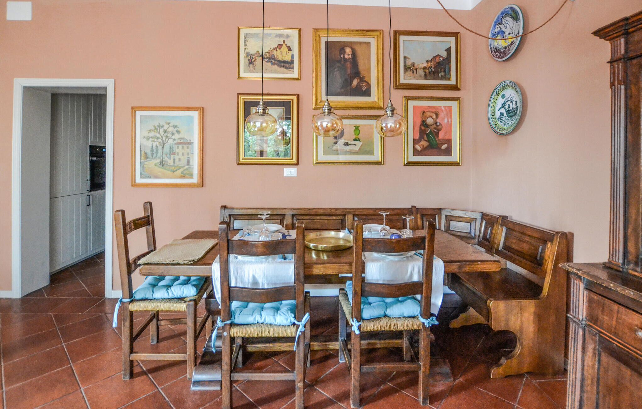 Un coin repas avec des chaises en bois et un banc, un sol carrelé et des œuvres d’art encadrées accrochées au mur.