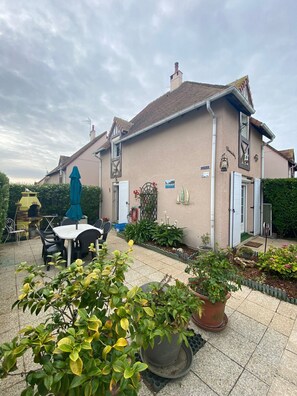 A building with a tiled patio, outdoor seating, and potted plants. - Chaleureuse Maison à la Plage (Courseulles-sur-Mer)