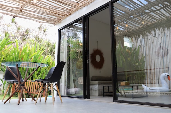 A modern outdoor seating area with a glass table and chairs, a decorative wreath, and a swan sculpture.