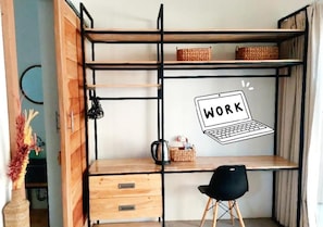 Compact workspace with a desk, chair, shelving unit, and potted plant.