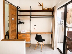 Habitación compacta con escritorio de madera, una silla, estante con toallas y puerta corredera.