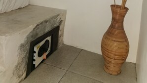 Et værelse med en seng, en stikkontakt på væggen, en lille elektronisk enhed og en vase med tørrede planter.