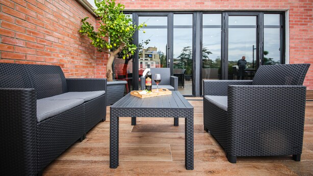 A patio area with wicker furniture, a table, and a potted plant.