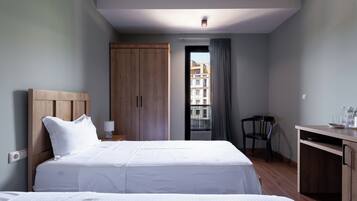 Habitación de hotel con una cama grande, un armario de madera, un escritorio con silla y vistas a edificios a través de una ventana.