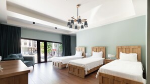 A hotel room with two wooden beds, a desk, and a view of the street through large windows.