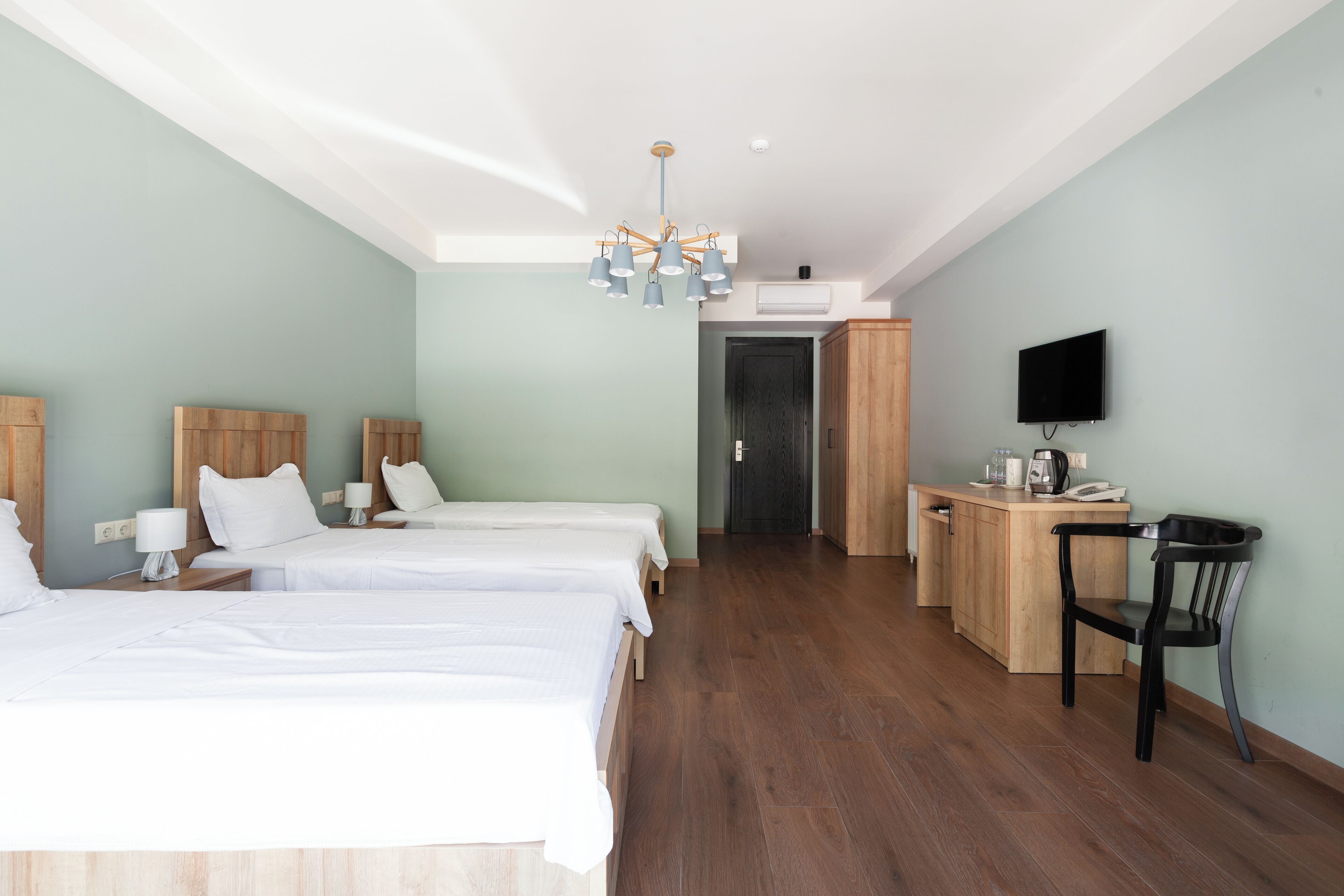 A hotel room with two beds, a desk, a chair, a television, and a wooden cabinet.