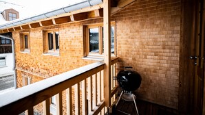 Un balcone in legno con una griglia, pareti in mattoni e una finestra.