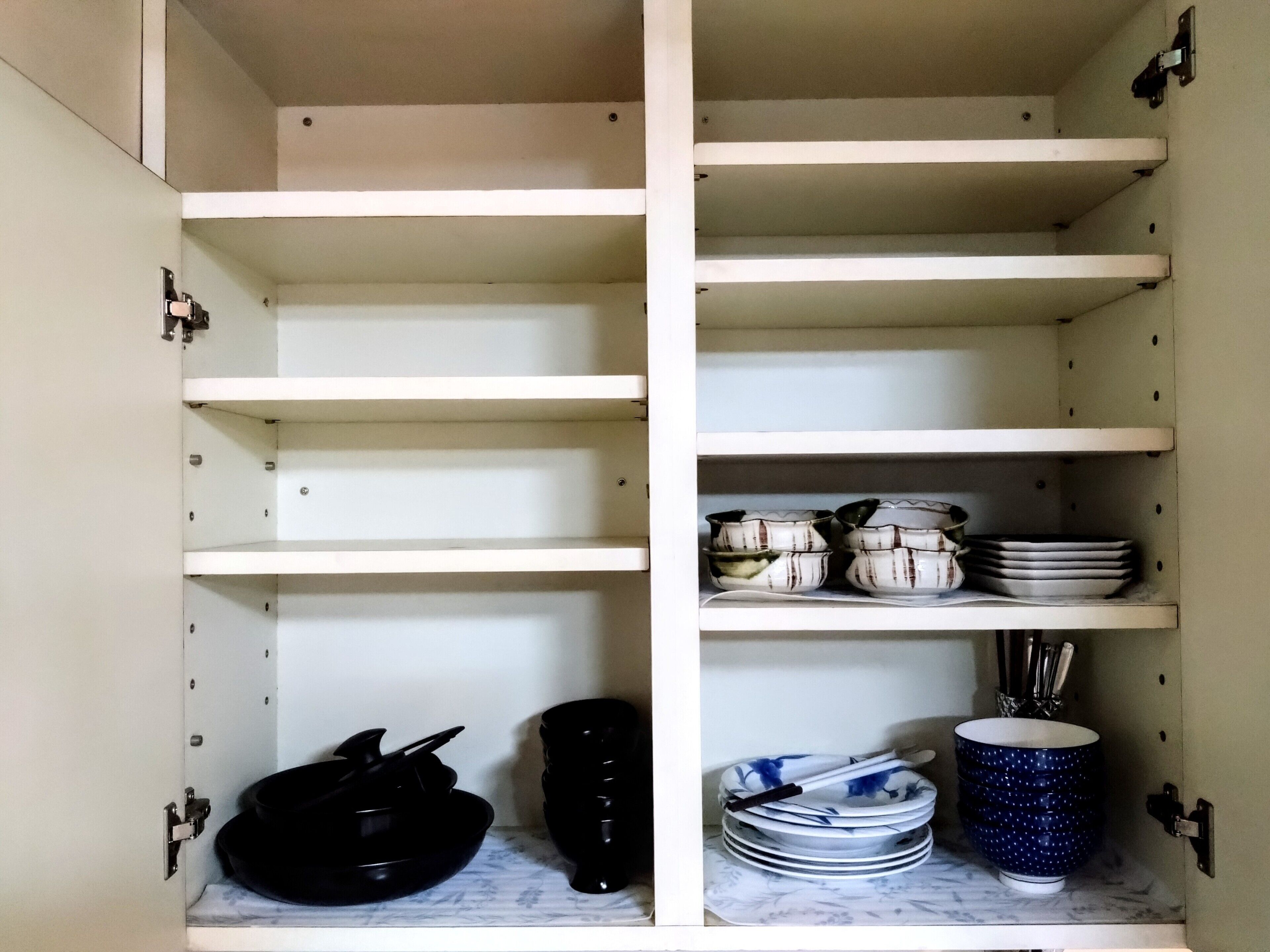 A kitchen cabinet with shelves, some of which are empty, and others holding kitchenware like bowls, plates, and a blue mug.
