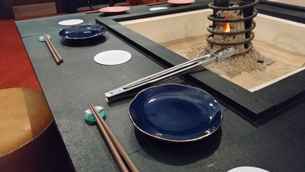 Una mesa de comedor con palillos, platos y una chimenea pequeña.