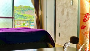 Habitación de hotel con cama, una mesa con una botella de vidrio y vista a un paisaje verde a través de la ventana.