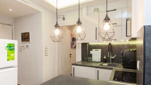 Een moderne keuken met een zwart aanrecht, een inbouwoven en een zwarte afzuigkap. Er hangen drie hanglampen met zichtbare gloeilampen.