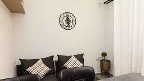 Een vergaderruimte met een ronde wandklok, twee banken met geruit kussens, een kleine bloempot en een grijze tafel.