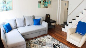 Een woonkamer met een grijze bank, een beige fauteuil, een kamerkleed met dessin en een trap.