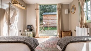 Un dormitorio con dos camas, una cabaña de madera visible a través de la puerta y una mesita con una lámpara.