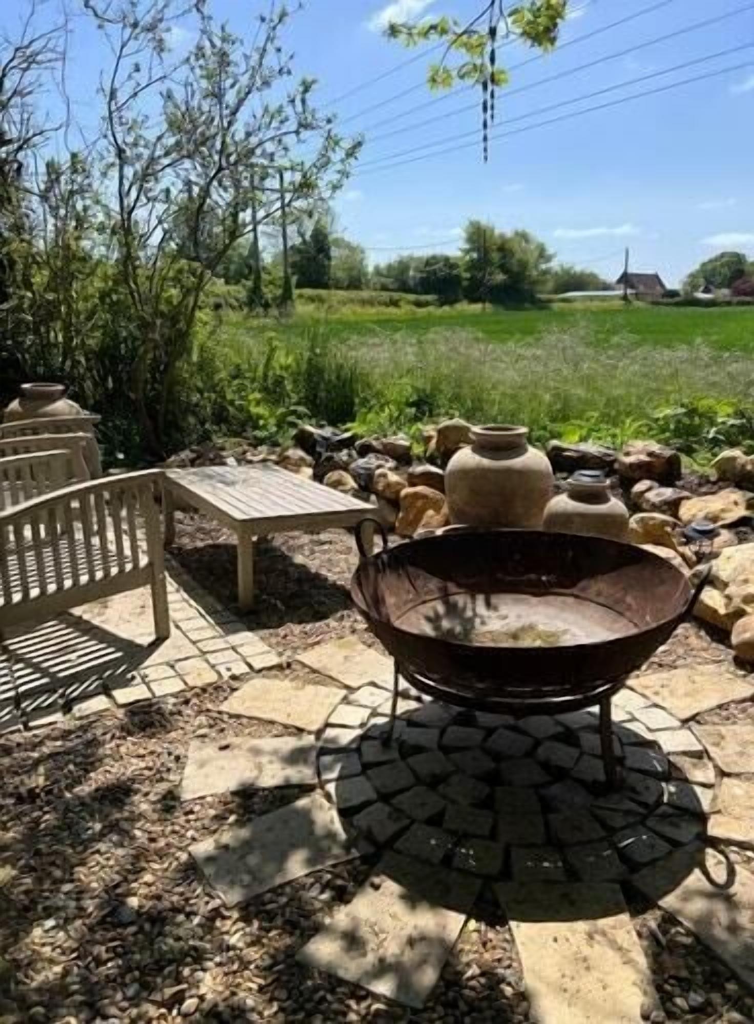 Een terras met een metalen vuurkorf, stenen tegels en een houten stoel.