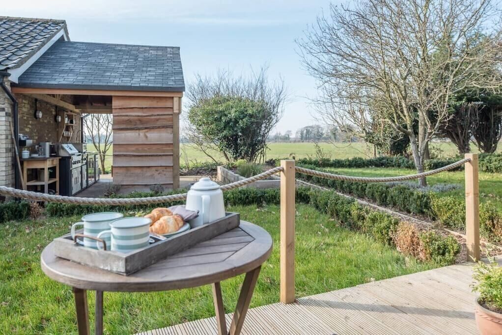 A rustic wooden cabin with a deck, a rope barrier, and a table with breakfast items.