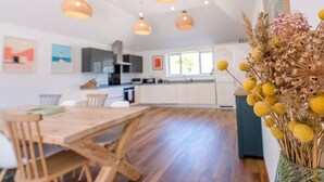 A modern kitchen with white cabinets, a wooden dining table, and pendant lighting. - Springfield, Westleton (Saxmundham)