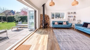 A modern living room with a large glass door leading to a patio, a blue sofa, a fireplace, and a view of the garden. - Springfield, Westleton (Saxmundham)