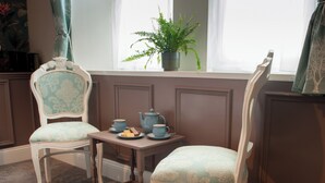 A room with two vintage-style chairs, a small table with tea set, and a window with a plant.