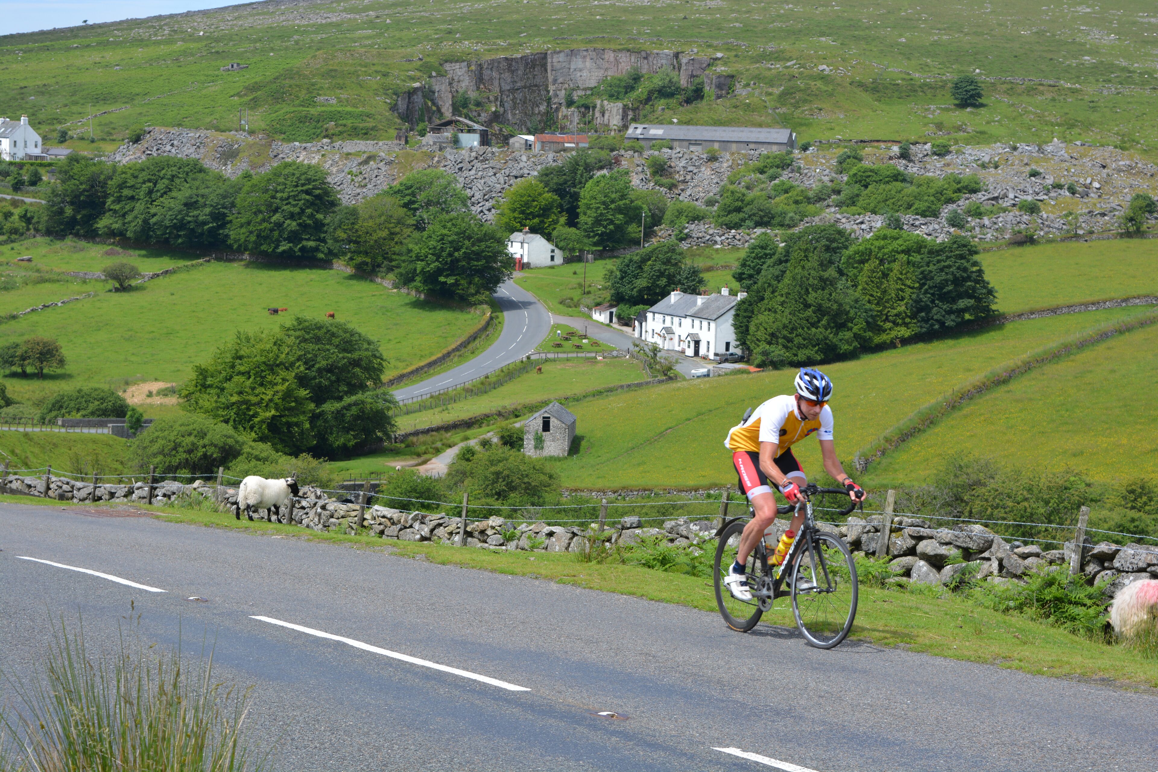A cyclist riding on a road with stone walls and greenery in the background.
