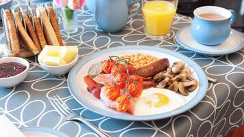 A breakfast table with a plate of eggs, sausages, beans, mushrooms, and tomatoes, accompanied by toast, butter, jam, and a glass of orange juice.