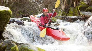 A person in a red kayak navigating a river with rocks and moss-covered stones.