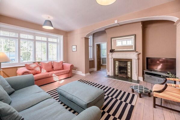 A living room with a pink sofa, blue armchair, and a fireplace.