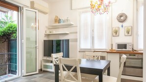 A modern kitchen with white cabinetry, a dining table with chairs, a flat-screen TV, a microwave, and a small oven. - BnButler - Riccardo Galli 9 (Milan)
