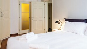 A neatly made bed with white linens, a bedside lamp, and a door with frosted glass panels. - BnButler - Riccardo Galli 9 (Milan)