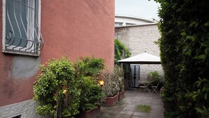 A courtyard with potted plants, a table and chairs, and a covered area. - BnButler - Riccardo Galli 9 (Milan)