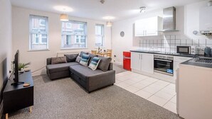 A modern apartment with a grey sofa, a small dining table, and a kitchen area with white cabinets and a red fridge.