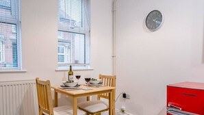 A small dining area with a wooden table and chairs, a clock on the wall, and a red cabinet.