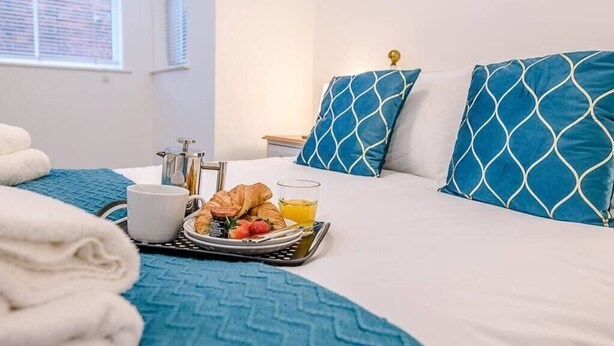 A neatly made bed with blue patterned pillows, a tray with croissants, strawberries, a cup, and a glass of orange juice.