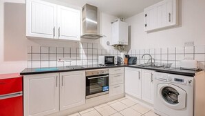 A modern kitchen with white cabinets, a stainless steel range hood, a microwave, an oven, a washing machine, and a red refrigerator.