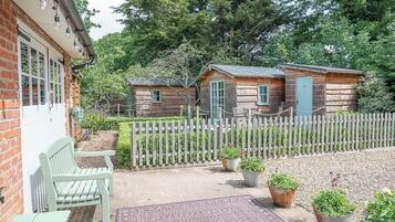 A rustic cabin with a wooden fence, a bench, and potted plants.