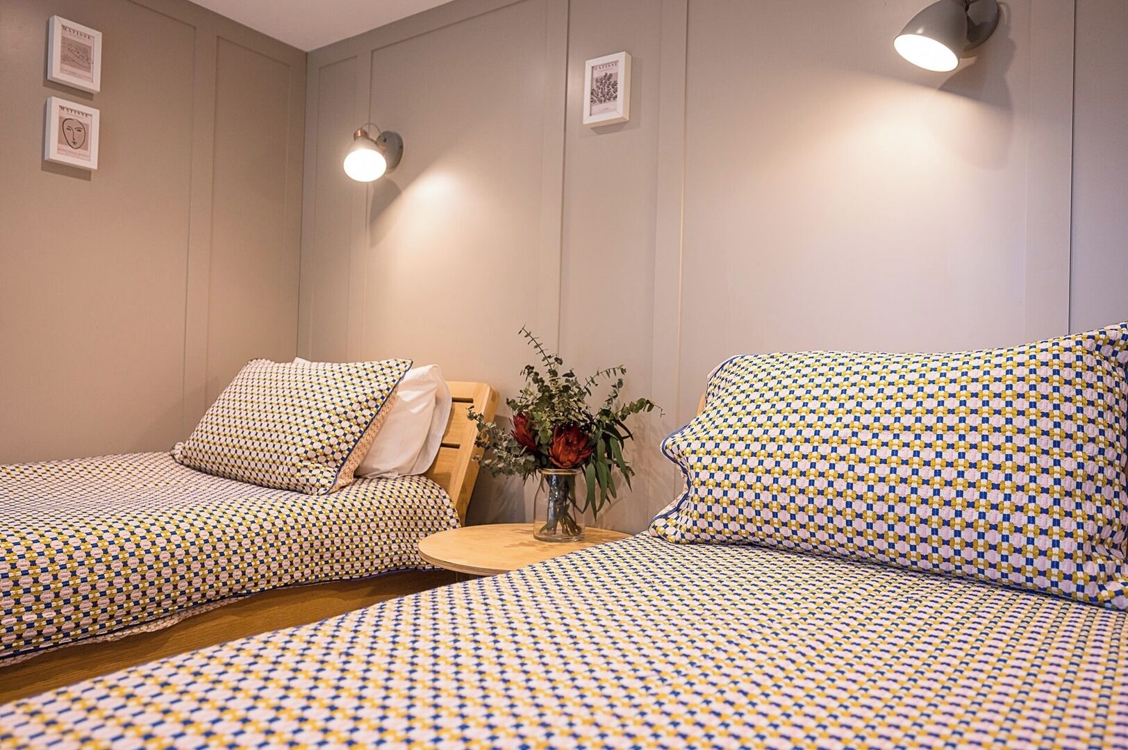 Una habitación con dos camas, una mesita con un florero y lámparas de pared.